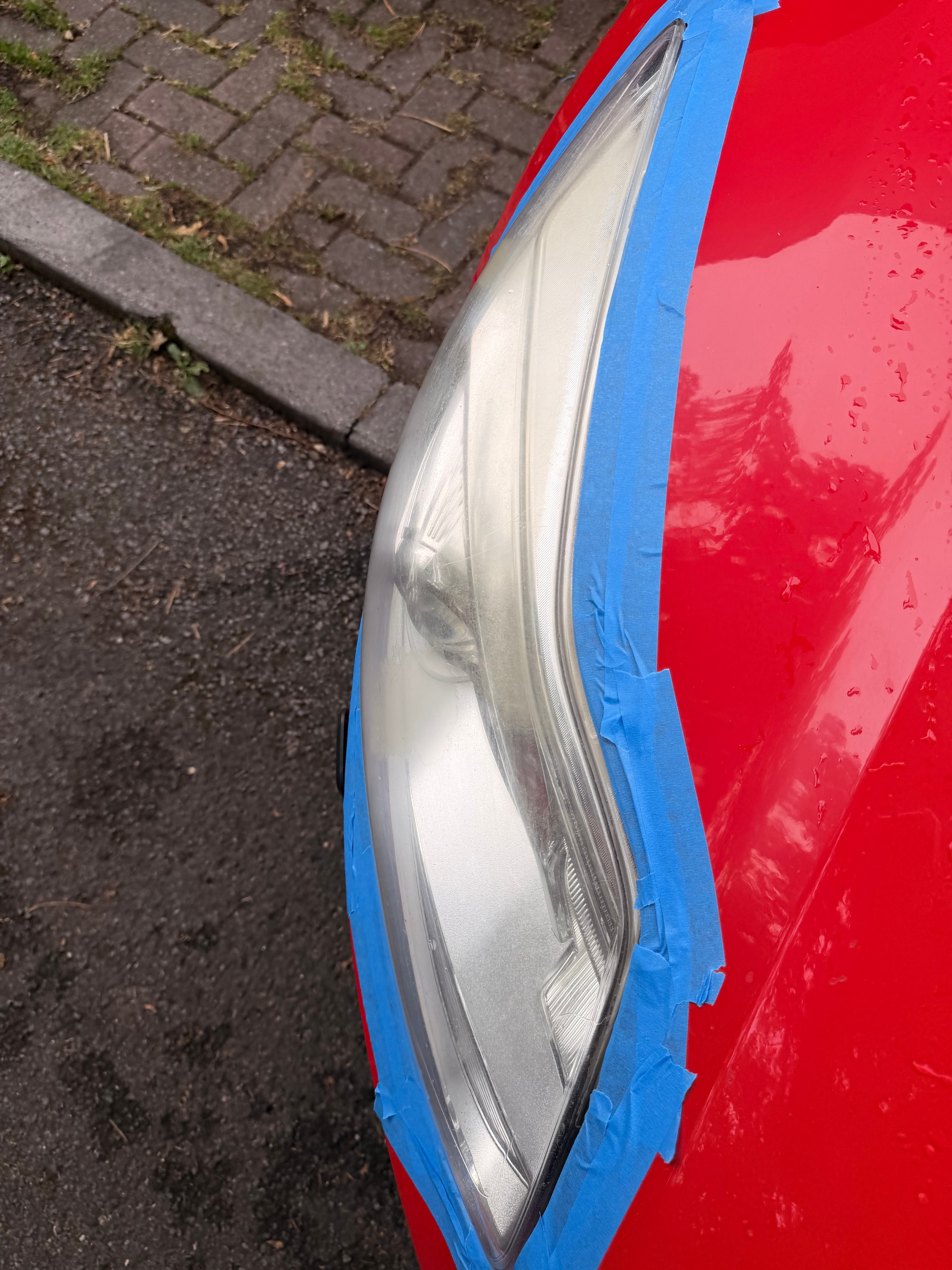 Red car headlight prepared for restoration with protective masking